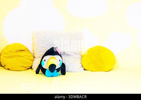 Toucan jouet mignon dans un intérieur jaune parmi des oreillers jaunes doux Banque D'Images