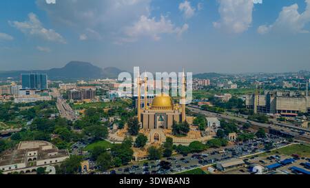 Vue aérienne de la Mosquée nationale, son dôme doré brillant au milieu d'une végétation luxuriante et de la vie urbaine animée, Abuja, Nigeria. Banque D'Images