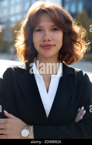 Femme d'affaires confiante aux bras croisés posant dans un environnement urbain moderne avec une attitude de leadership. Banque D'Images
