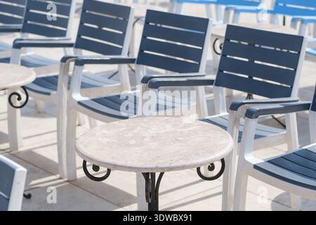 Coin salon extérieur avec plusieurs chaises longues bleues et blanches disposées autour d'une petite table ronde par une journée ensoleillée Banque D'Images