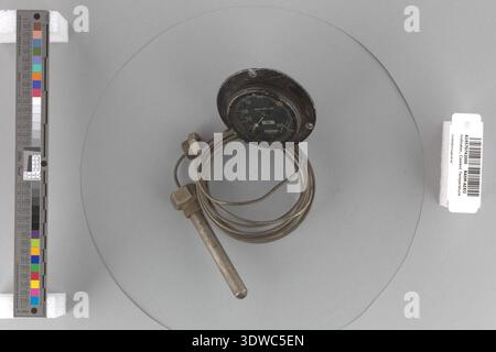 Indicateur de température du liquide de refroidissement CA. 1918 est un instrument de moteur conçu pour mesurer la température du liquide de refroidissement dans les premiers systèmes de combustion interne. L'appareil mesure 54 mm de diamètre et 30 mm de profondeur, avec un cadran argenté sur noir de 2-1/4 pouce et une large bride de montage. L'image d'archives documente la face de jauge circulaire et le boîtier métallique typiques de l'instrumentation mécanique de l'époque de la première Guerre mondiale. Banque D'Images