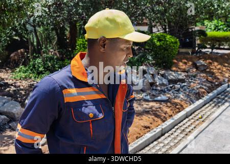 travailleur de la construction africain souriant portant une chemise bleue et une casquette jaune ouvrier gros plan portrait à l'extérieur Banque D'Images