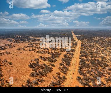 Drone aérien éloigné de la nature sauvage africaine Botswana, région du Kalahari, capture une route de gravier sans fin qui s'étend dans l'horizon, entourée par des espar secs Banque D'Images