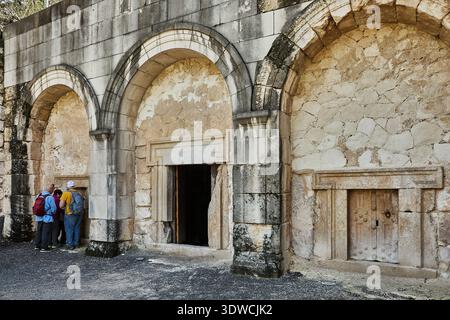 Touristes explorant d'anciennes tombes en pierre avec des entrées voûtées sur le site archéologique dans la région méditerranéenne, entouré par un terrain rocheux et Banque D'Images