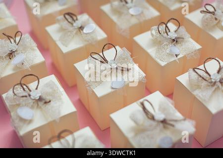 Les boîtes beiges ornées de dentelle blanche, de noeuds bruns et de petites roses, chacune arborant des étiquettes ovales, sont soigneusement disposées sur un fond rose pastel. Ces d Banque D'Images