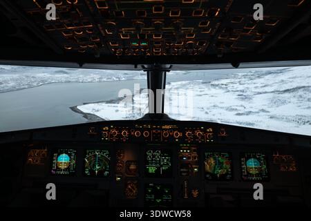 Commandes et écrans du cockpit tout en survolant un paysage enneigé et de l'eau Banque D'Images