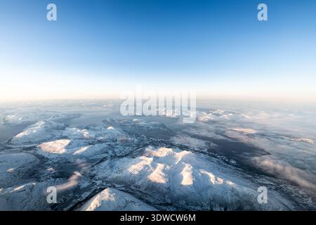 Vue aérienne mettant en évidence un vaste paysage hivernal immaculé avec des sommets ensoleillés et des fjords sereins Banque D'Images