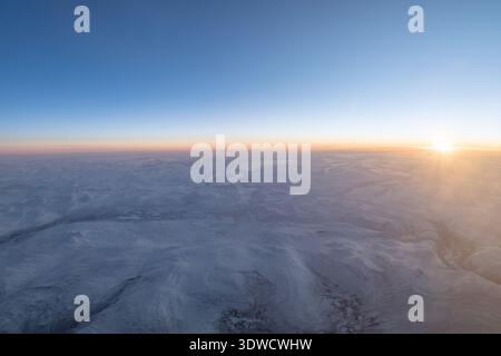Vue aérienne mettant en valeur un vaste paysage arctique enneigé avec un soleil levant Banque D'Images