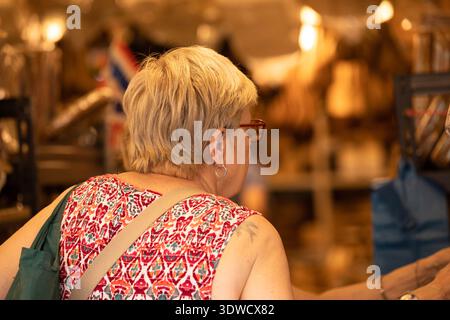 BANGKOK, THAÏLANDE. JAN 25 2026 : femme senior explorant dans le marché, intersection piétonne urbaine, vue arrière, au marché de Chatuchak. Banque D'Images