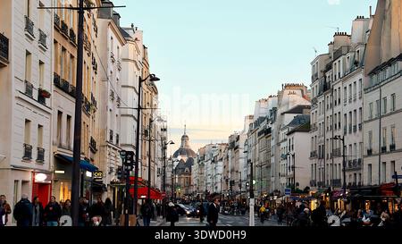 Vue typique de la rue à Paris, France avec des voitures sur la route et des gens marchant le long du trottoir. Ambiance urbaine authentique de la capitale française sho Banque D'Images