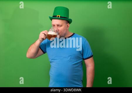 Homme buvant de la bière tout en portant un chapeau de leprechaun vert. – Toast festif de Patricks Day. Célébration des fêtes irlandaises et photographie de tradition pub Banque D'Images