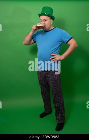 Homme buvant de la bière de la tasse tout en portant un chapeau vert. – Patricks Day Irish Celebration. Plaisir festif de vacances et plaisir décontracté. photographie Banque D'Images