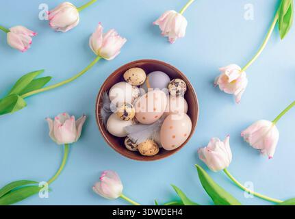Fond festif de Pâques de bol avec des œufs peints et des tulipes roses sur fond bleu. Vue de dessus, pose à plat. Banque D'Images