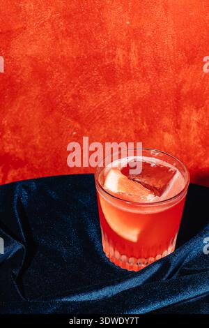 Un cocktail Negroni classique présenté dans un verre avec un grand glaçon et une tranche d'orange, sur un fond orange vif et un luxueux Fab sombre Banque D'Images