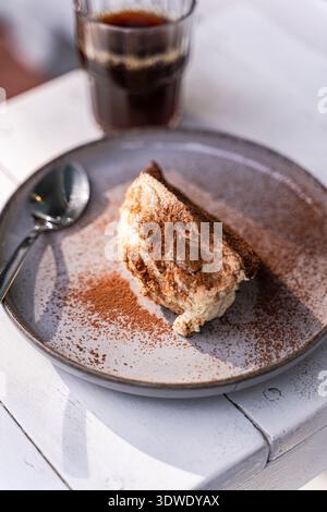 Une délicieuse tranche de tiramisu saupoudrée de cacao repose sur une assiette rustique, accompagnée d'un verre de café. La combinaison parfaite pour un des délicieux Banque D'Images