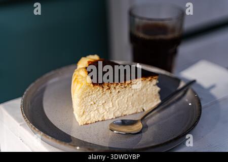 Une délicieuse tranche de cheesecake basque servie sur une élégante assiette grise, accompagnée d'une tasse de café fraîchement infusé, créant une paire de desserts parfaite Banque D'Images