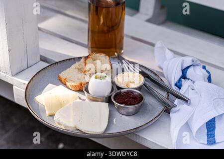 Une assiette de petit-déjeuner avec du fromage tranché, un œuf dur, du pain, du beurre et de la sauce se trouve sur une table. L'arrangement offre un début simple mais délicieux Banque D'Images