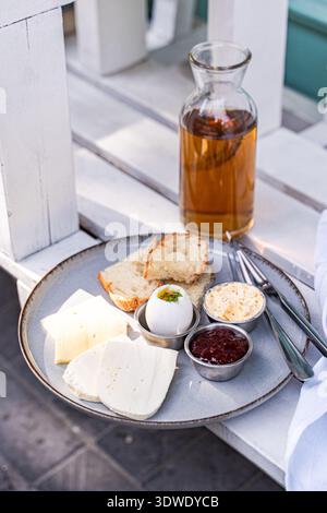 Une assiette de petit-déjeuner avec du fromage tranché, un œuf dur, du pain, du beurre et de la sauce se trouve sur une table. L'arrangement offre un début simple mais délicieux Banque D'Images