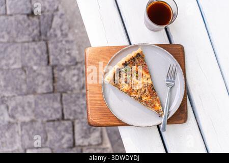 Une délicieuse tarte aux champignons, délicatement disposée à la fourchette sur une assiette en céramique, servie sur une planche de bois. Cette tarte cuite au four est parfaite pour profiter de l'outdo Banque D'Images