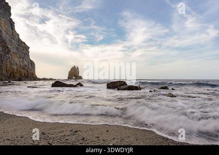 Paysage côtier avec de puissantes vagues s'écrasant sur des rochers déchiquetés sous un ciel partiellement nuageux. La scène capture la beauté sauvage et dynamique natu Banque D'Images