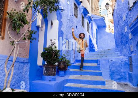 Un homme explore joyeusement les rues bleues vibrantes de Chefchaouen, au Maroc, capturant le charme unique et l'essence culturelle du célèbre Blue C. Banque D'Images