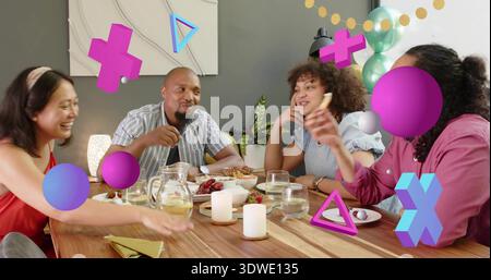 Bavarder quatre amis portant des dessus partageant de la nourriture à une table en bois avec des bougies, des ballons et des superpositions Banque D'Images