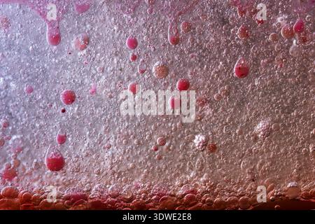 Un plan macro artistique de bulles chatoyantes dans un liquide coloré, mettant en valeur un mélange fascinant de teintes roses et violettes. L'image met en évidence la texture Banque D'Images