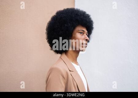 Un profil latéral d'une personne avec une coiffure afro volumineuse portant un blazer brun élégant, debout contre une toile de fond bicolore, mettant en valeur l'élégance Banque D'Images