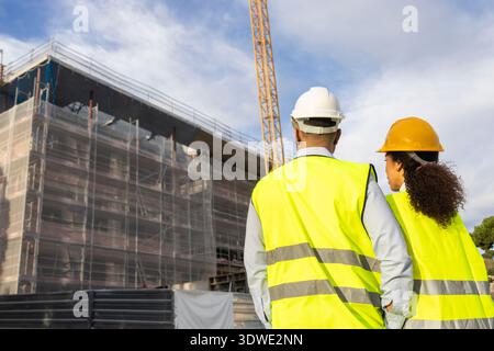 Deux ingénieurs en construction, portant des gilets de sécurité et des casques, surveillent l'avancement d'un chantier. La structure est dans les premiers stades avec échafo Banque D'Images