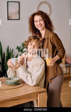 Un joyeux couple aux cheveux bouclés partage des verres et des rires dans leur élégant appartement. Banque D'Images