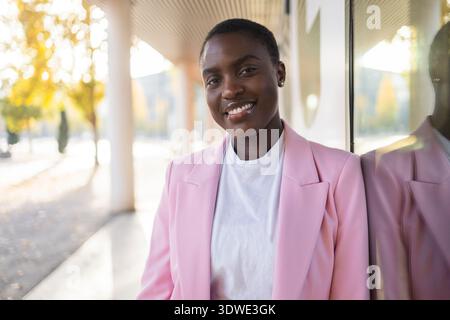 Portrait d'une femme d'affaires africaine confiante et PDG, souriant brillamment dans un cadre extérieur. Vêtue d'un élégant blazer rose, elle se tient comme un ins Banque D'Images