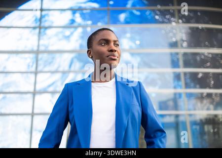 Femme d'affaires africaine dans un blazer bleu se tient en toute confiance à l'extérieur d'un bâtiment moderne. Elle respire le leadership et la détermination, incarnant le rôle de A. Banque D'Images