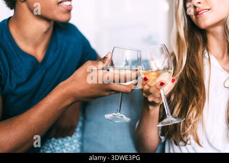 Un couple multiethnique profite d'un moment cosy à la maison, en serrant des lunettes pour un toast. Leur atmosphère détendue met en valeur l'unité et la célébration, capturant Banque D'Images