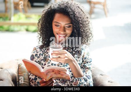 Une femme profite d'une matinée paisible, assise sur un canapé confortable avec une tasse de café chaude à la main, alors qu'elle se plonge dans un livre engageant dans Bright nat Banque D'Images