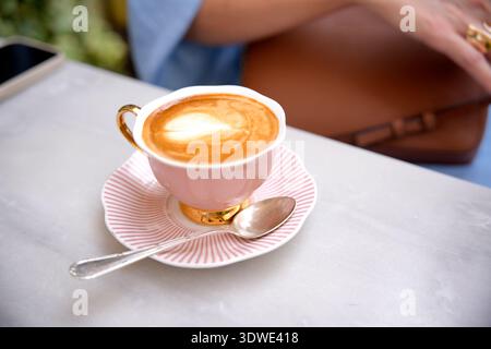 Femme recadrée méconnaissable est assise dans un café, sa main reposant sur une table à côté d'une tasse de café fumante sur une soucoupe rayée, créant un invi confortable et confortable Banque D'Images