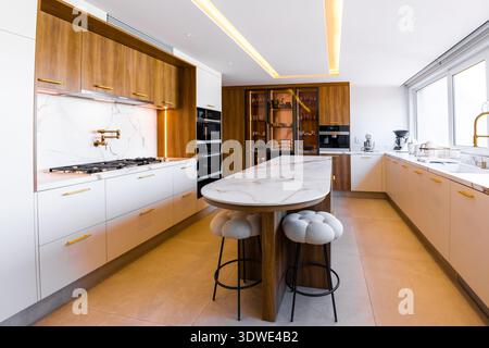 Superbe cuisine de luxe avec un îlot de marbre élégant, des appareils modernes et des armoires en bois élégantes. Les grandes fenêtres offrent lumière naturelle, highlightin Banque D'Images