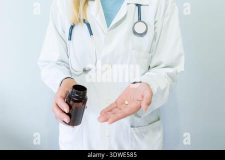 Médecin féminin recadré méconnaissable dans un manteau blanc tenant une bouteille de produit pharmaceutique et distribuant des pilules dans sa main, illustrant les soins de santé et M. Banque D'Images