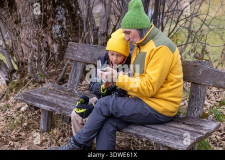 Un moment chaleureux entre grand-père et petit-fils assis sur un banc rustique. Ils se lient sur un intérêt commun pour la nature au cours d'une journée d'automne paisible en t Banque D'Images