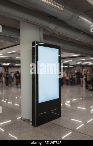Un grand écran numérique se trouve bien en vue dans un terminal d'aéroport animé. L'arrière-plan présente des voyageurs qui attendent ou partent, encap Banque D'Images