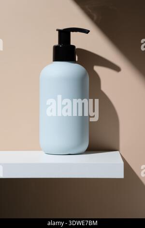 Un flacon cosmétique épuré et minimaliste avec distributeur à pompe noir se trouve élégamment sur une étagère blanche. Il est parfait pour ranger des lotions, des crèmes ou autres Banque D'Images