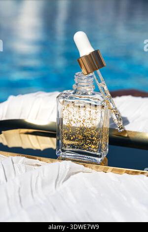Installation cosmétique élégante avec un sérum chatoyant dans un flacon compte-gouttes transparent. Parfait pour les soins du visage et du corps, soulignant après les soins solaires et dorés Banque D'Images