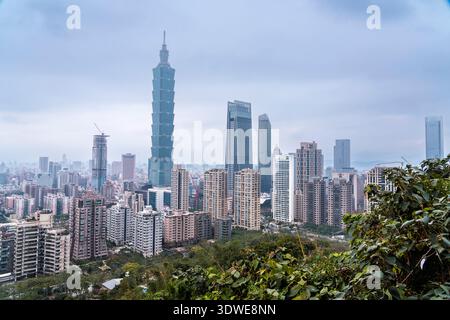Vue surélevée de Taipei, Taïwan, avec l'emblématique gratte-ciel Taipei 101 au milieu du paysage urbain animé. Verdure luxuriante au premier plan ajoute un nat Banque D'Images