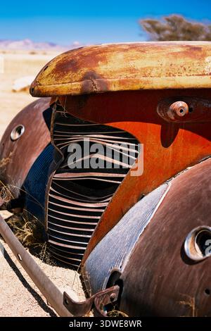 Gros plan d'une grille de voiture d'époque rouillée avec une patine altérée, sur un paysage désertique aride. Le soleil projette des ombres, mettant en évidence le u de la voiture Banque D'Images