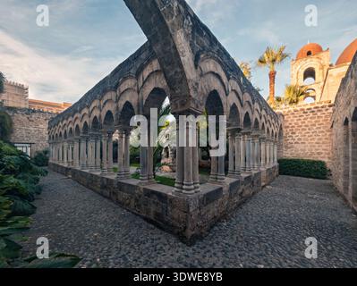 Une belle vue sur les arches de pierre historiques dans une ancienne cour de cloître à Palerme. La scène est rehaussée par des palmiers et des chemins pavés en dessous Banque D'Images