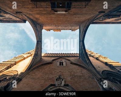 Vue captivante sous un bâtiment historique de Palerme, présentant des détails architecturaux complexes et le ciel bleu clair. Les structures en pierre Banque D'Images