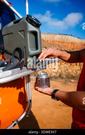 Aventure à Red Canyon, Espagne. Une personne verse de l'eau dans une cafetière à partir d'un récipient portable, mettant en évidence l'exploration en plein air et les ressources Banque D'Images