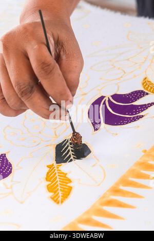 Un artisan qualifié applique délicatement de la peinture sur le tissu, mettant en valeur l'art complexe de la fabrication du batik en Indonésie. La vue rapprochée révèle le Precisi Banque D'Images