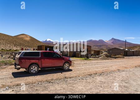 Un SUV rouge garé sur un chemin de terre dans un village isolé de Catamarca, en Argentine, sur fond de collines et de montagnes sous un ciel bleu clair. Rus Banque D'Images