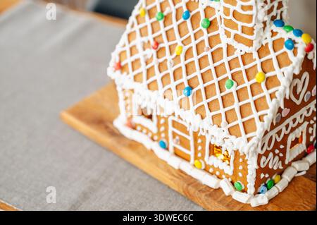 Une maison en pain d'épice joliment décorée, ornée de bonbons colorés et de glaçage blanc, se trouve sur une planche de bois, incarnant l'esprit de Noël an Banque D'Images