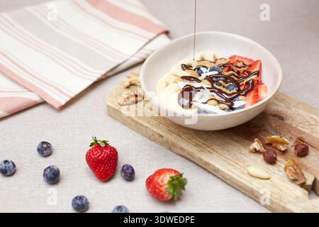 Un bol de petit déjeuner délicieux et nutritif avec des fraises fraîches, des bananes et des bleuets, arrosé de chocolat, parfait pour commencer votre journée Banque D'Images